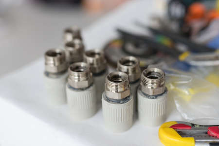 Combined couplings for connecting metal and polypropylene water pipes on desktop. Nuts in warm colorsの写真素材