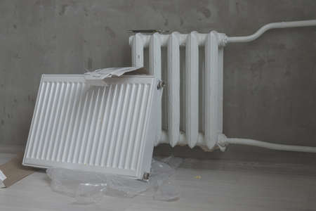 Heating battery on the gray wall. Horizontal photo of white metal heater new and old radiator