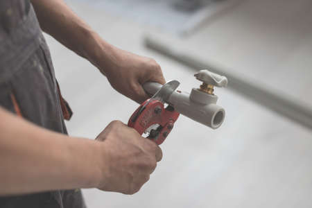 Close-up of hand with red scissors cut pipes for heating, or water supply. Polypropylene pipe with tap with blurred backgroundの写真素材