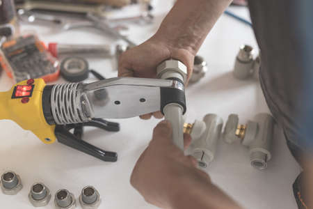 Man keep soldering iron for polypropylene. Close-up of hand with yellow iron and pipes for heating or water supplyの写真素材