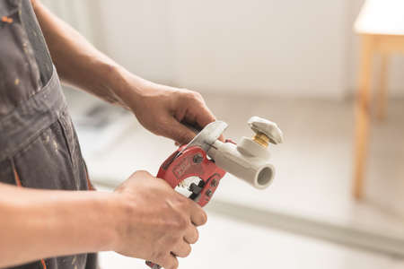 Close-up of hand with red scissors cut pipes for heating, or water supply. Polypropylene pipe with tap with blurred background