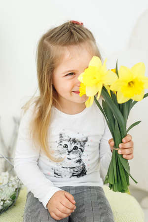 Close up of little girl with yellow flowers. Portrait of happy child in white blouse look in cameraの写真素材