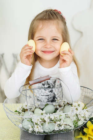 Portrait of little girl with Easter basket and yellow eggs . Smiling child in white blouse look in cameraの写真素材