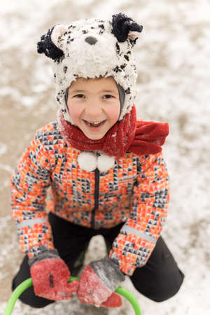 Portrait of smiling boy child in snow look in camera. Close up of happy boy wear red gloves and black white hat outdoorの写真素材