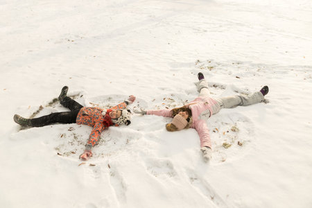 Happy family lying on snow and make angel. Mother and son child playing having fun together in winter weatherの写真素材