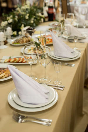 Close up of festive table setting with wine glasses, fresh flowers on beige tableclothの写真素材