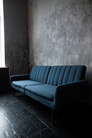 Blue sofa in a room with concrete wall and black floor background.