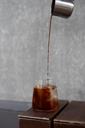 Coffee pouring into a glass with ice cubes on wooden table
