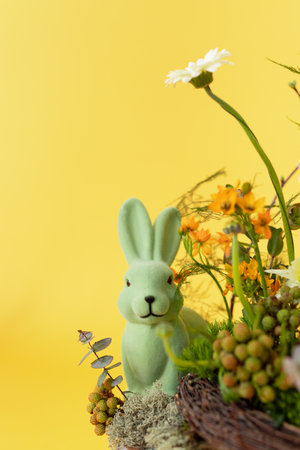 Easter decoration with rabbit and flowers on yellow background. Copy space.