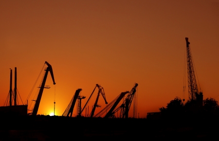Silhouette of sea port cranes over sunsetの写真素材