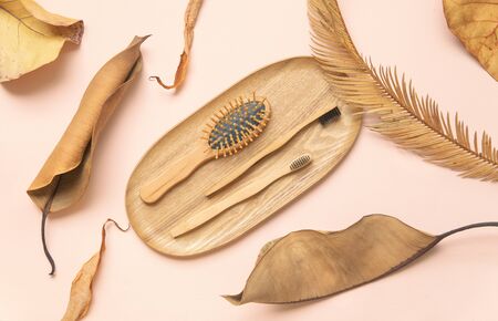 Flatlay design of morning accessories, toothbrush, hairbrush on bamboo plate with dry tropical...