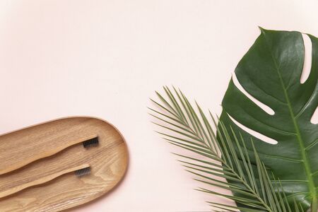 Flatlay design of morning accessories, toothbrush, hairbrush on bamboo plate with green tropical leaves on pink background with text place.の写真素材