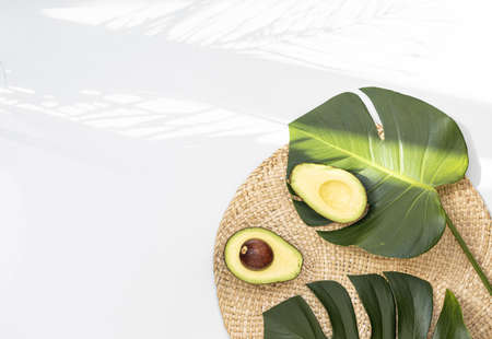 Avocado pieces on a natural fibers floor and has a background of nature. Tropical monstera leaf.