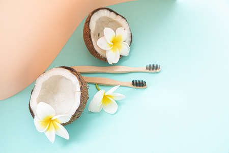 Bamboo toothbrush and coconut on a table with copy space on a pastel background. Styled composition of flat lay with tropical flowers.の写真素材