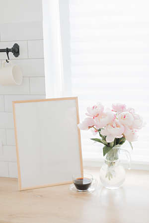 Vertical frame mockup on a wooden table in the kitchen. Glass vase with a bouquet of pink peonies...