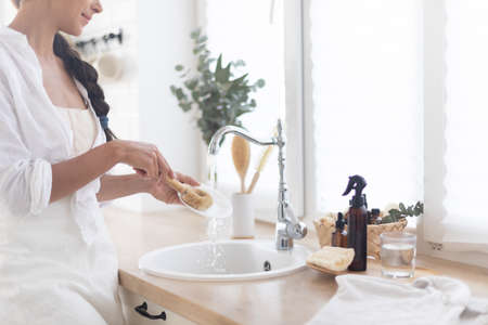 Woman washing dishes with detergent on kitchen. Eco brush with foam and basket on white bright kitchen.の写真素材