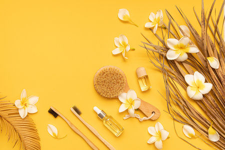 Bamboo toothbrush and dried palm leaf oil on a table with copy space on a yellow background. Styled composition of flat lay with tropical leaves and flowers.の写真素材