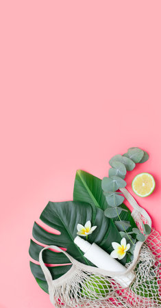 Tropical palm tree leaf and eco bag on a pink background. Sunscreen and hat in composition with monstera leaves.Vibrant minimal fashion conceptの写真素材