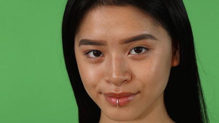 Sliding cropped shot of a stunning young beautiful Asian woman smiling joyfully to the camera, posing on green chromakey background, copy space. Beauty, skin, skincare, health concept.の写真素材