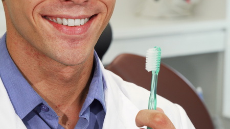 Cropped shot of a handsome male dentist in labcoat smiling, showing off his healthy white teeth, holding a toothbrush. Cheerful professional dentist posing with a toothbrush.の写真素材