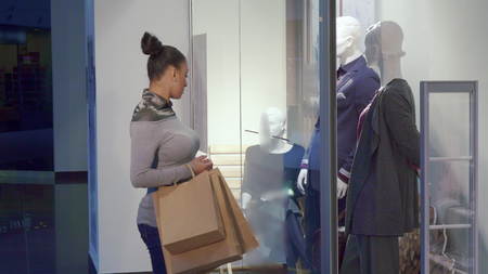 Attractive african american woman coming to the store window. Pretty brunette lady shopping at the...