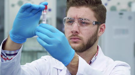 Young brunette man looking at the test-tube at the laboratory. Close up of atractive male scientist frowning. Brunette caucasian lab worker examining some testの写真素材