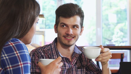 Close up shot of a young cheerful handsome man talking to his girlfriend while having coffee together at the local cafe. Lovely couple relaxing at the coffee shop, having breakfast.の写真素材