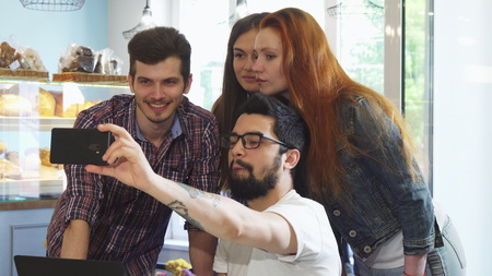 Young bearded handsome man using his smart phone taking selfies with a group of his friends at the...