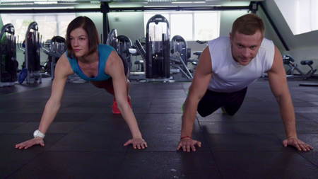Fitness man and woman doing push ups at the gym. Sportsman and sportswoman synchronously raising and...