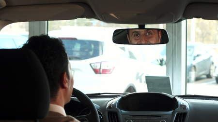 The car is in the parking lot. The man adjusts the air conditioning and mirrors. Then he looks into...