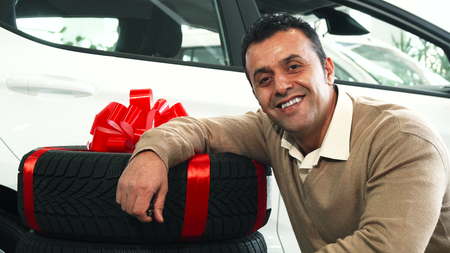 A man comes to the new wheels. He puts his hand on them and sits next to them. He looks at the camera and smilesの写真素材