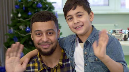 Little brunette boy and his father waving their hands. Attractive african american man and his son looking into the camera. Close up of handsome guy with his male kid against background of christmas treeの写真素材