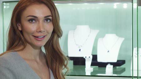 Close up of a stunning red haired sexy young beautiful woman examining showcase at the jewelry store smiling to the camera copyspace beauty femininity shopping consumerism retail purchasing.の写真素材