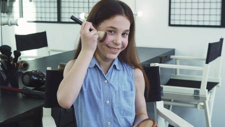 Cute cheerful little girl smiling applying makeup having fun pretending to be an adult beauty fashion cosmetics face skin flawless artist visage femininity posing playful growing up actress.の写真素材