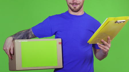 Cropped shot of a professional deliveryman smiling cheerfully delivering postal order holding cardboard box with copyspace and clipboard on green background profession employee post concept.の写真素材