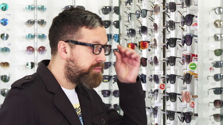 Profile shot of a bearded mature man trying on glasses in front of the mirror shopping for eyewear at the optometrist store consumerism retail customer eyes sight healthy vision.の写真素材