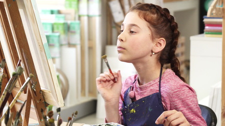 Adorable cheerful little girl examining her painting smiling to the camera showing thumbs up enjoying art class at her school childhood creativity children drawing imagination joy.の写真素材