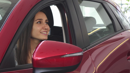 Cheerful young attractive woman sitting in her newly bought automobile smiling happily receiving car...