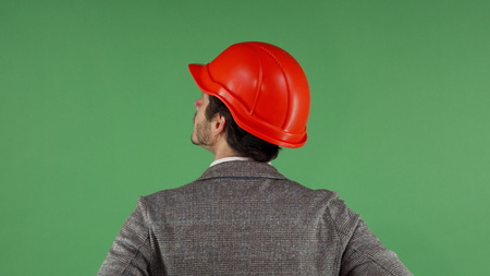 Cropped rear view shot of a male engineer in protective hardhat looking at the green chromakey...