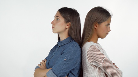 Two female friends standing back to back looking angry after having a fight. Young women looking annoyed and upset after quarreling. Disagreement, friendship conceptの写真素材