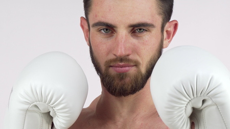 Bearded male boxer smiling to the camera, standing in fighting stance. Confident fighter holding up his hands in boxing gloves, ready to fight. MMA, martial arts, defense conceptの写真素材