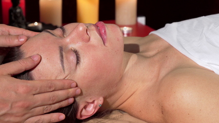 Lovely young woman enjoying face massage with her eyes closed. Cropped shot of a woman resting at spa center, during head massage. Skincare, rejuvenation, cosmetology conceptの写真素材
