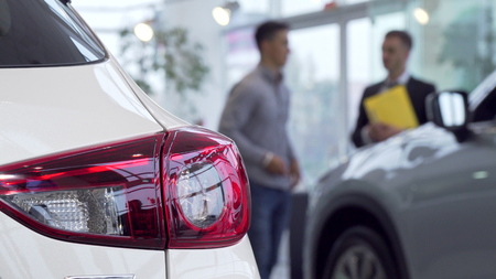 Car lights on the foreground, man buying car at the dealership on the background. Selective focus on a car, salesman helping male customer on the background. Buying car conceptの写真素材