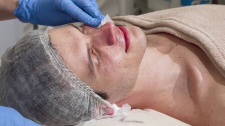 Professional cosmetologist cleaning skin of a male client with cotton pad. Cropped shot of a man getting skincare facial treatment by beautician. Skin, relaxation conceptの写真素材