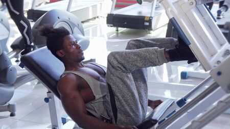 Athletic young African man working out on leg press machine at the gym. Handsome ripped strong male...