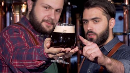 Selective focus on a glass of dark beer in hands of a brewer. Two professional beer makers...