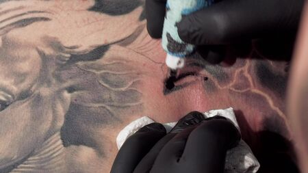 Cropped macro shot of a tattooist using tattoo machine, making tattoos. Sliding cropped shot of a...