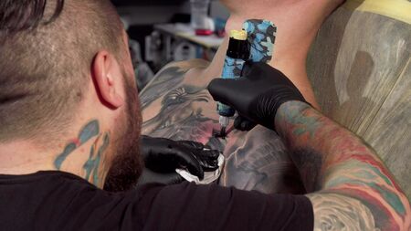 Rear view shot of a tattoo artist making a tattoo on chest of a male customer. Cropped shot of unrecognizable man getting his chest tattooed by professional tattooistの写真素材