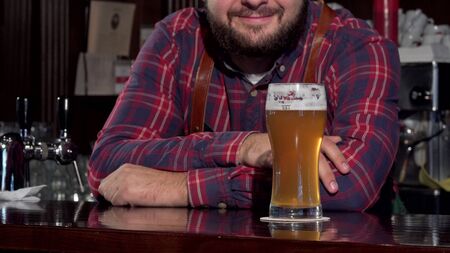 Unrecognizable bartender smiling, putting glass of beer on the counter. Cropped shot of a bartender serving you delicious craft beer in a glass, smiling joyfully. Service, celebration conceptの写真素材