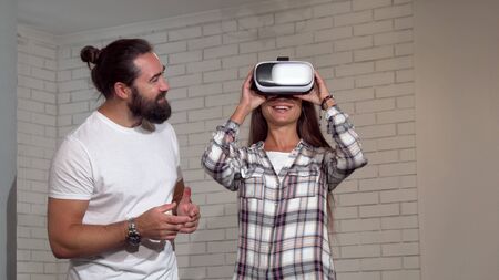 Handsome bearded man watching his girlfriend using virtual reality glasses. Beautiful woman wearing...